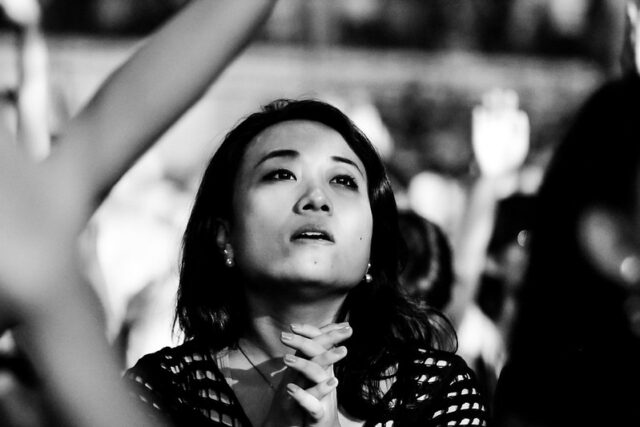 Black and white photograph of woman looking up, her hands clasped.