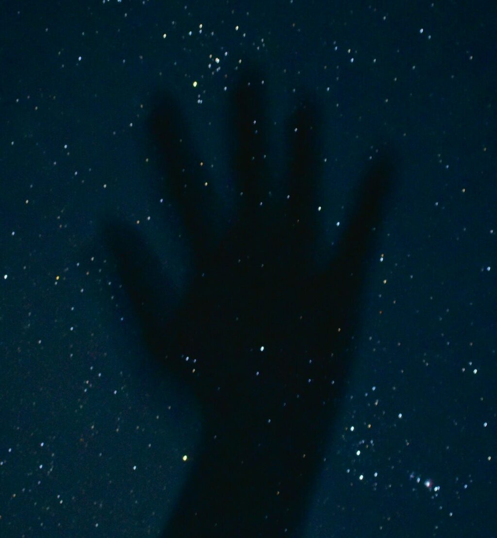 Photograph of an upraised palm (hand) against a backdrop of stars.