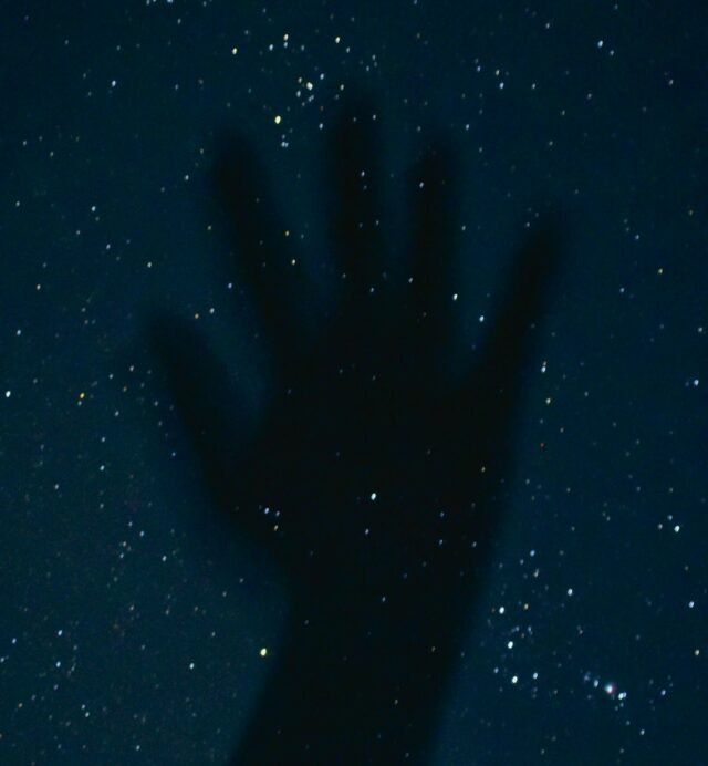 Photograph of an upraised palm (hand) against a backdrop of stars.