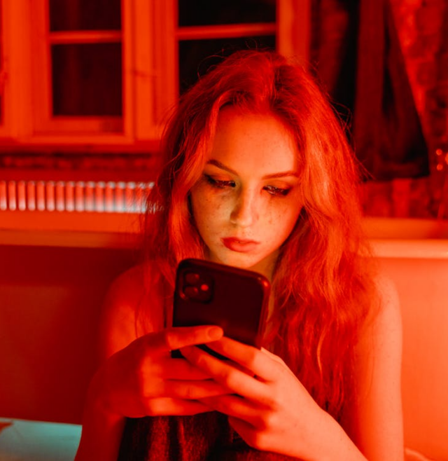 Image of young woman looking at her phone in an obsessive manner.