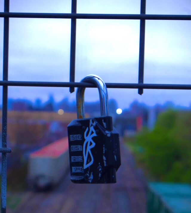 Image of a combination lock attached to a fence, above a rail yard.