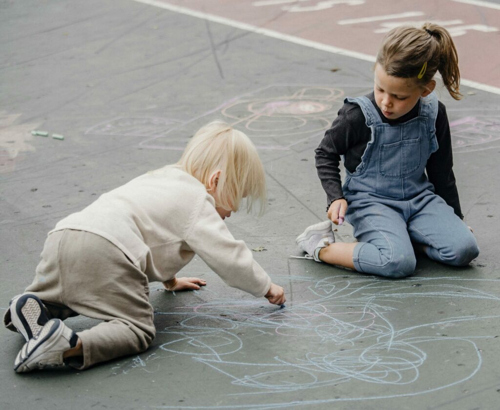 Two young children drawing on the ground with chalk.