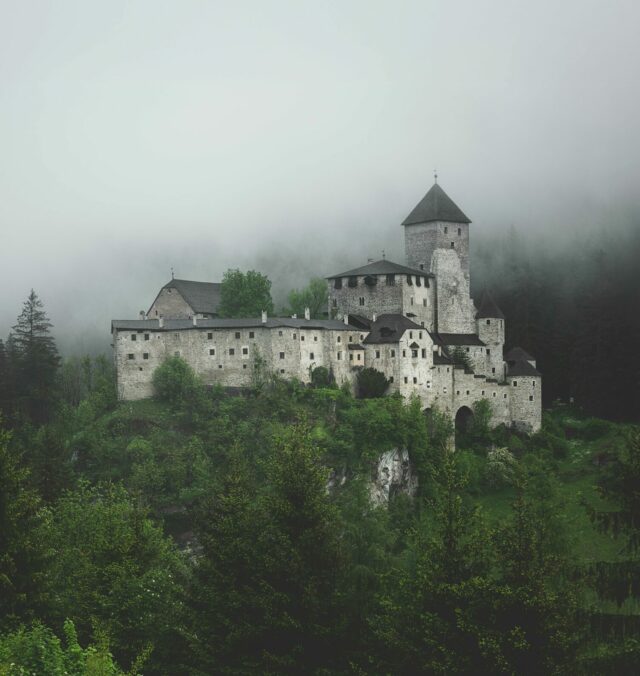 Photograph of a castle on a green hill, surrounded in fog.