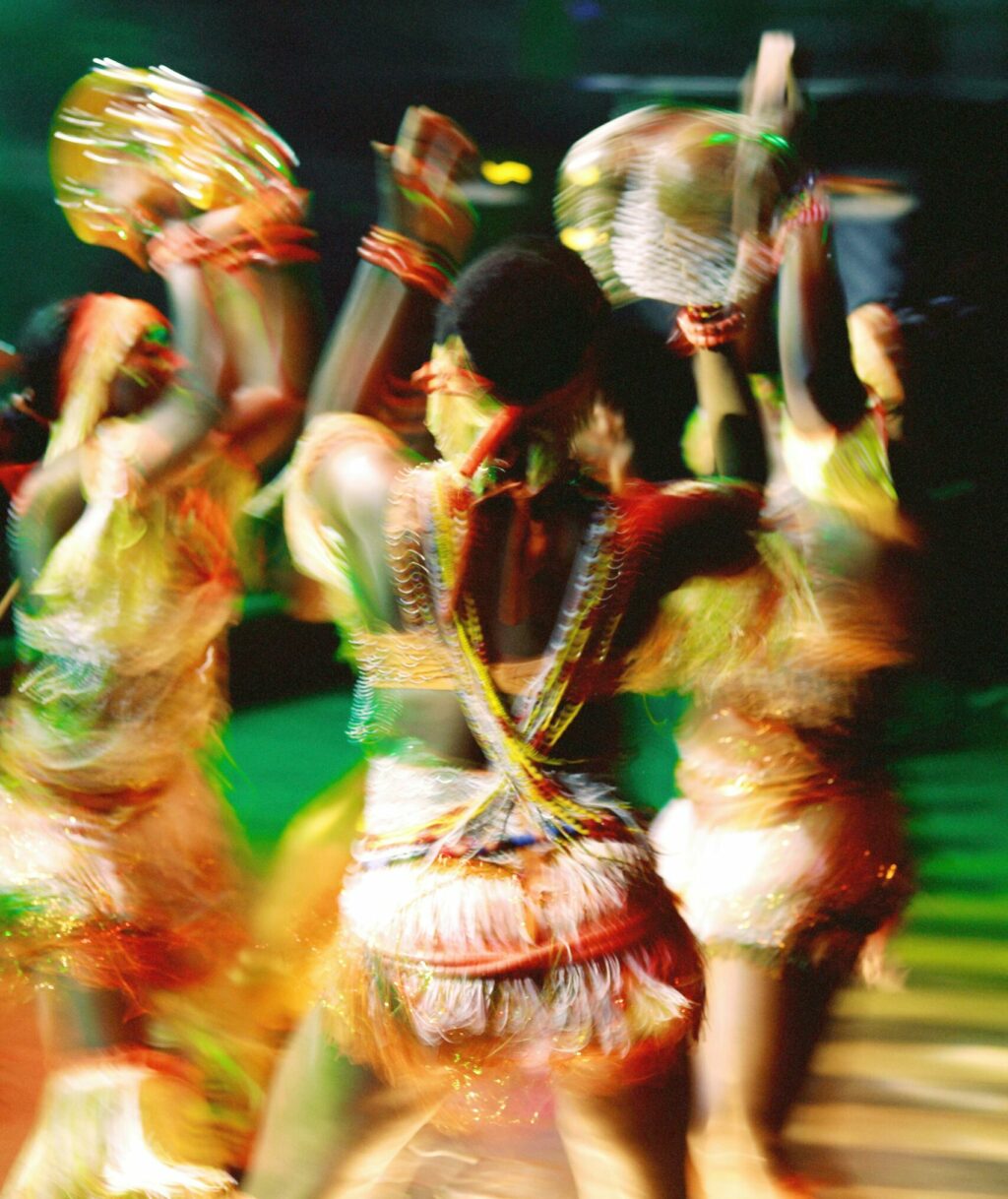 Blurred, highly saturated color photograph of women dancing in a circle with their hands aloft.